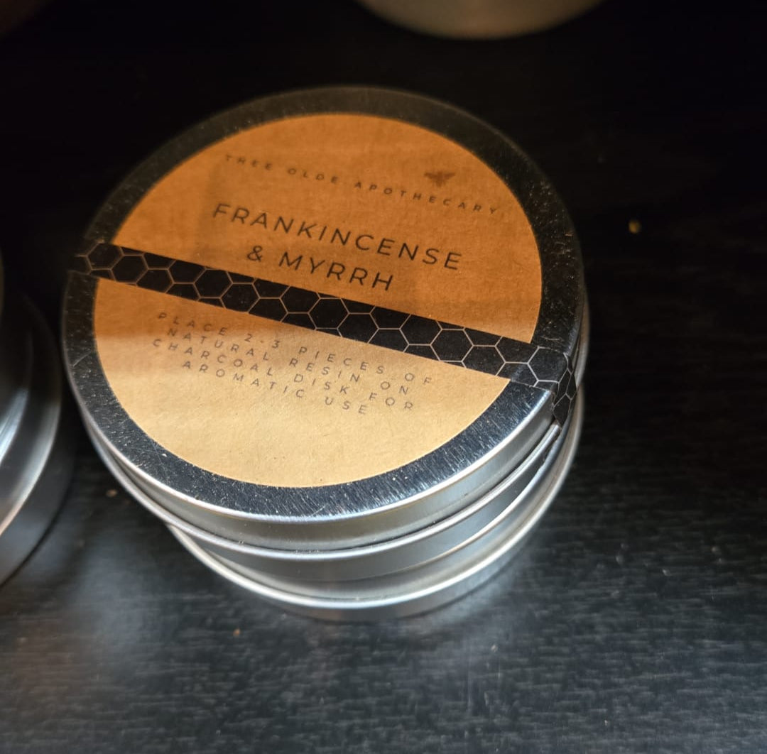 Stack of small containers labeled 'Frankincense & Myrrh' on a dark surface.
