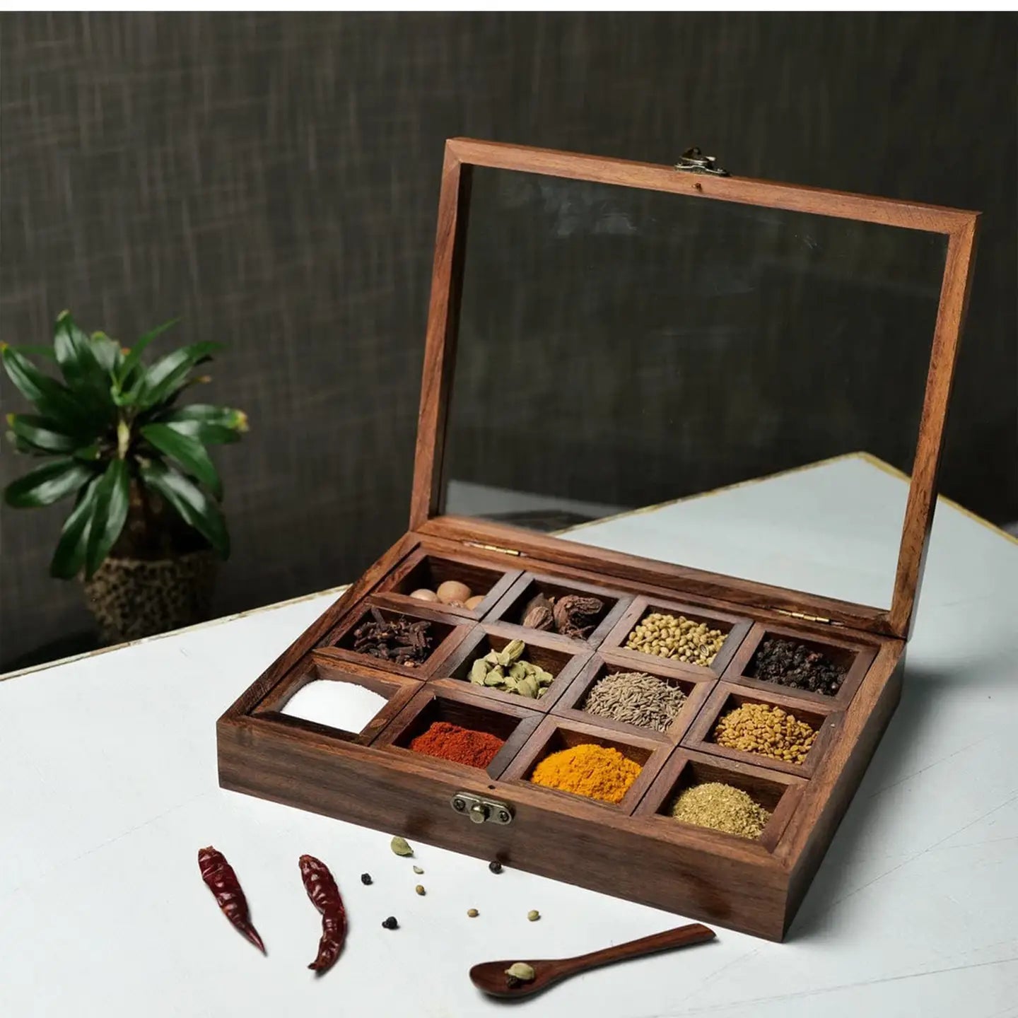 Wooden spice box with transparent lid containing various spices on a white surface.